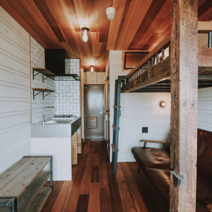 木板貼りの天井とソファとロフトベッドのあるワンルーム